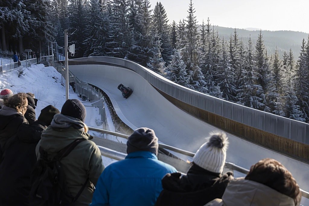 Vereiste Steilkurve einer Bobbahn mit Zuschauern am Absperrgitter an einem sonnigen Wintermorgen
